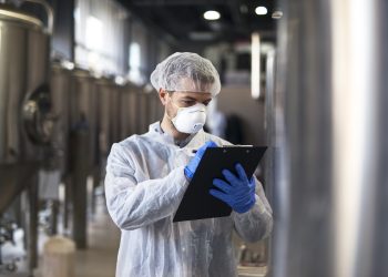 Technologist in white uniform checking quality in industrial production factory.