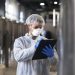 Technologist in white uniform checking quality in industrial production factory.