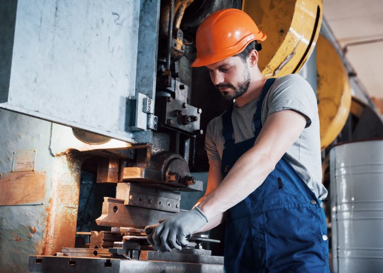 Portrait of a young worker in a hard hat at a large metalworking plant. The engineer serves the machines and manufactures parts for gas equipment