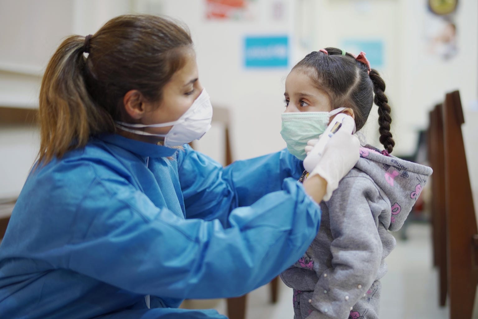 nurse wearing ppe taking temperature of a child at phc center