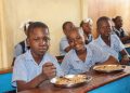 Niños haitianos reciben alimentos en un centro escolar apoyado por Mary's Meals, mientras la organización lanza un llamamiento urgente ante la crisis alimentaria.
